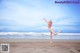 A woman in a bikini jumping in the air on a beach.