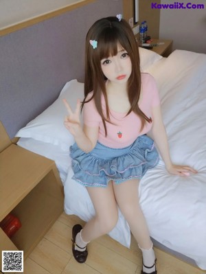 A woman in a pink shirt and blue skirt sitting on a bed.