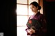 A woman in a kimono holding a fan in front of a window.