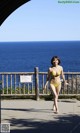 A woman in a yellow bikini walking by the ocean.