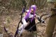 A woman with purple hair holding a sword in the woods.