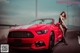 A woman sitting on top of a red convertible car.