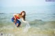 A woman in a red top and blue skirt standing in the water.